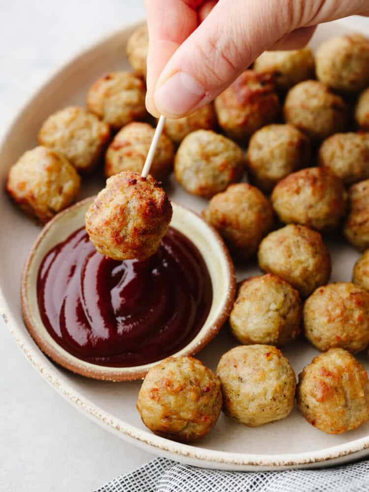 A meatballs with a toothpick being dipped into BBQ sauce.